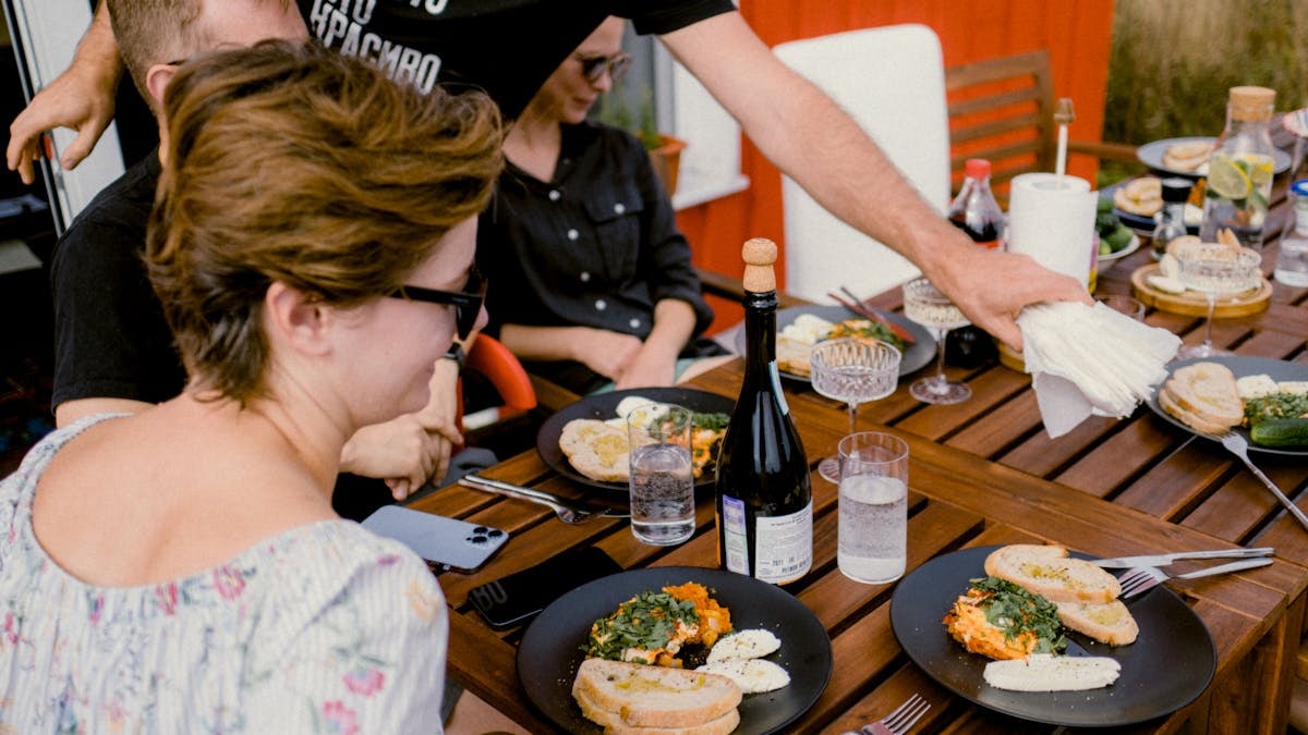 Group enjoying a meal with herbs and eggs on a wooden terrace, creating a vibrant social setting.